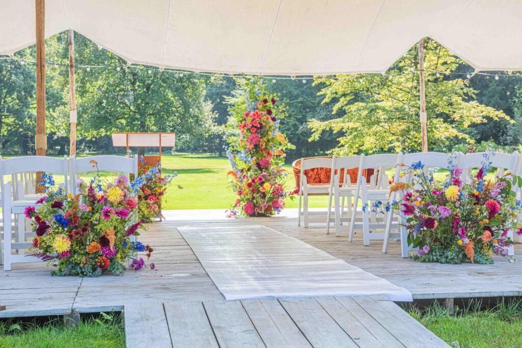 Outdoor trouwceremonie met bloemen en witte stoelen